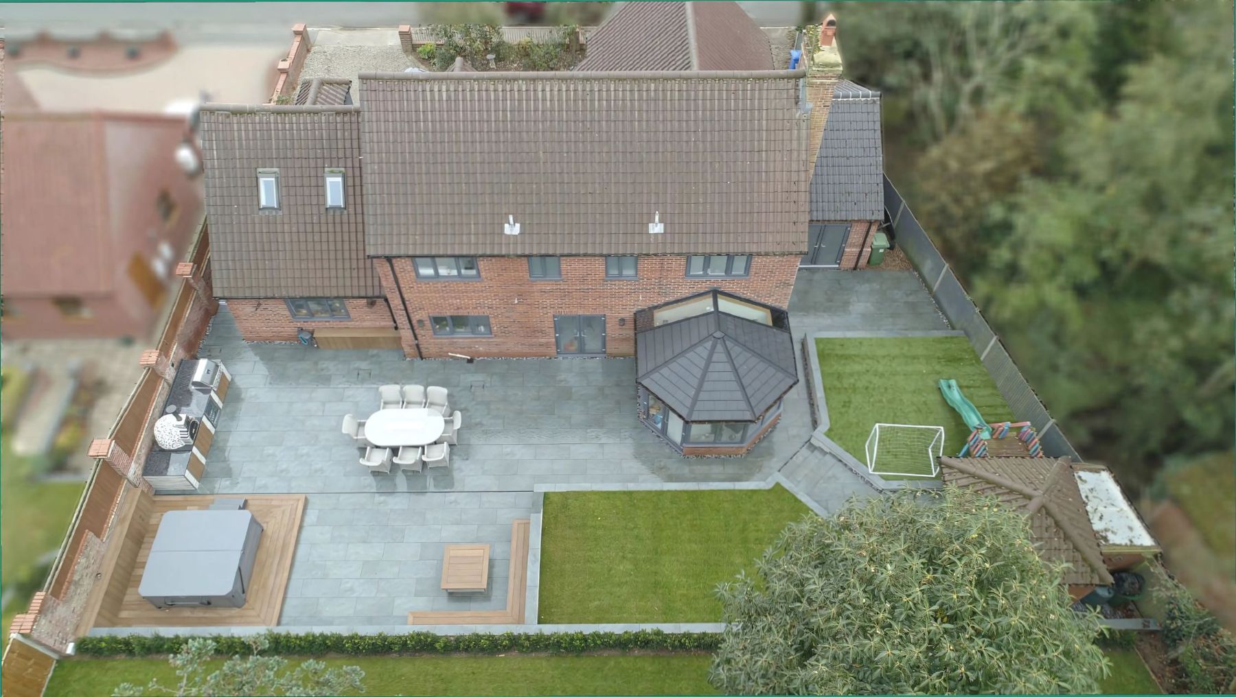 Aerial view of a finished garden with a grey patio, gazebo, lawns and planting beside a brick house