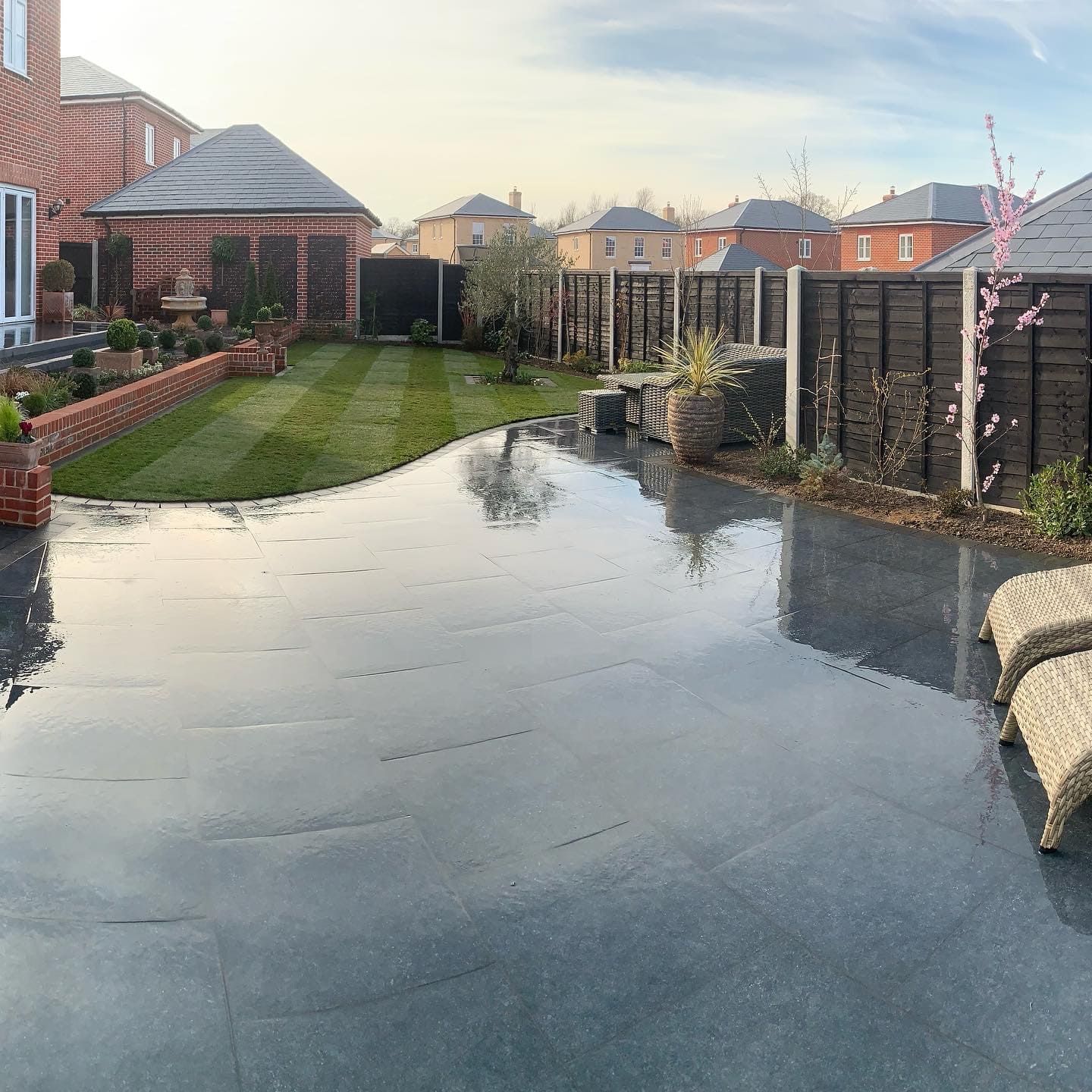 Black porcelain patio curving round a lawn after rain