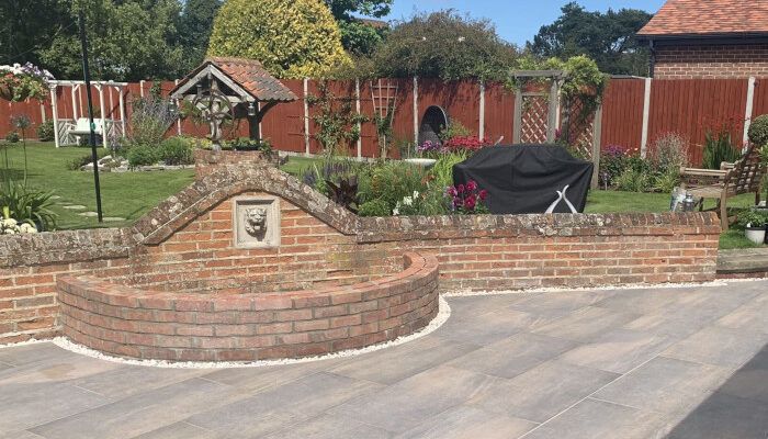 Porcelain patio laid around a curved brick wall with a water feature