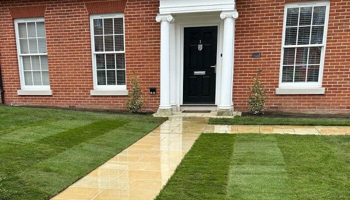 Fresh turf and a sandstone path in front of a red brick house