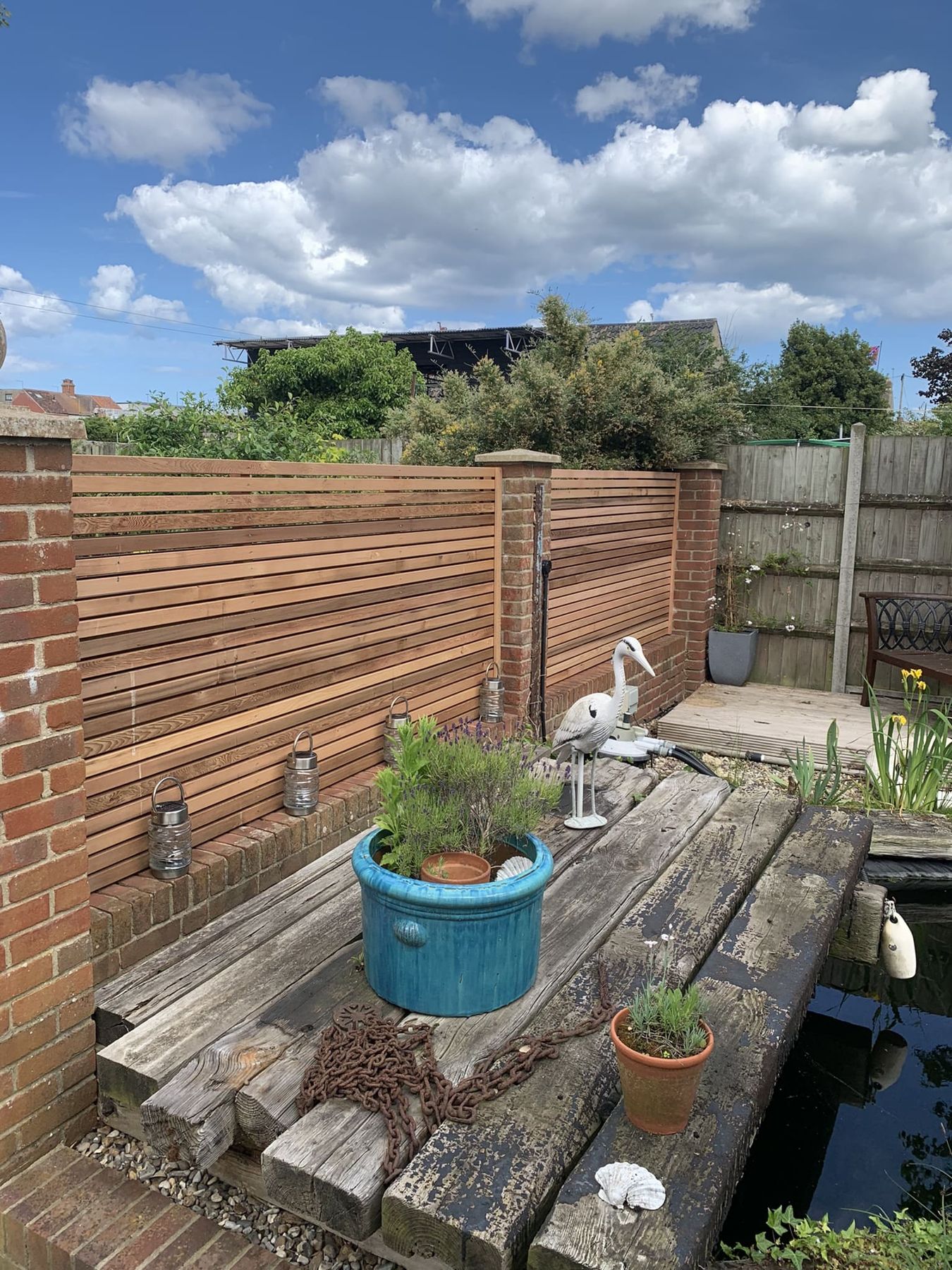 Slatted cedar screening above a pond edged with sleepers