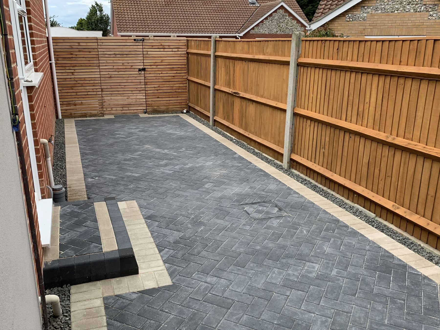 Charcoal herringbone block path beside a closeboard fence