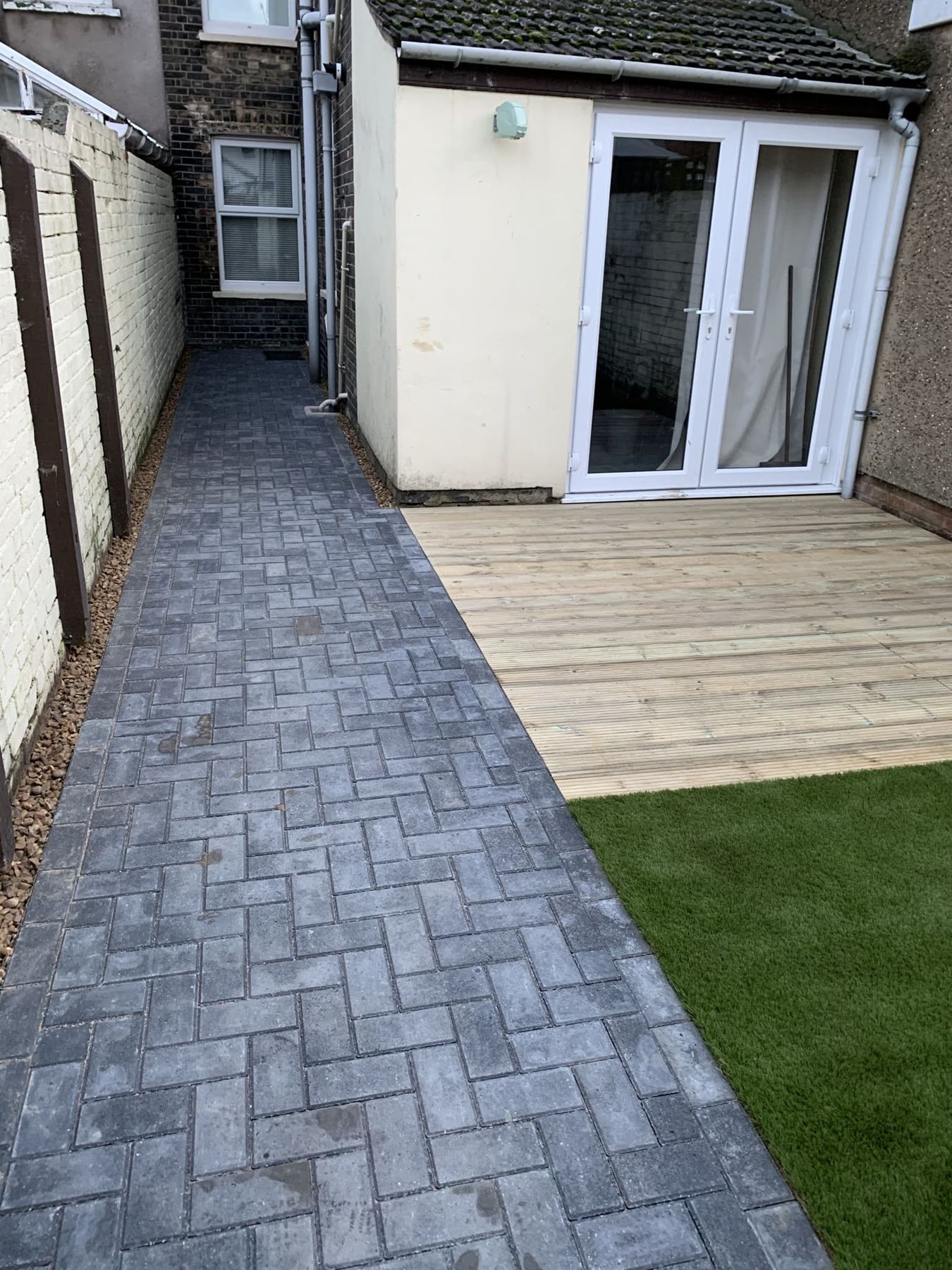 Charcoal block paving path leading to decking and a lawn