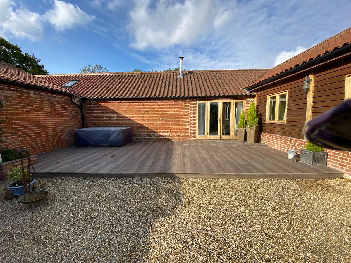 Dark composite decking laid against a brick and timber barn conversion with a gravel courtyard