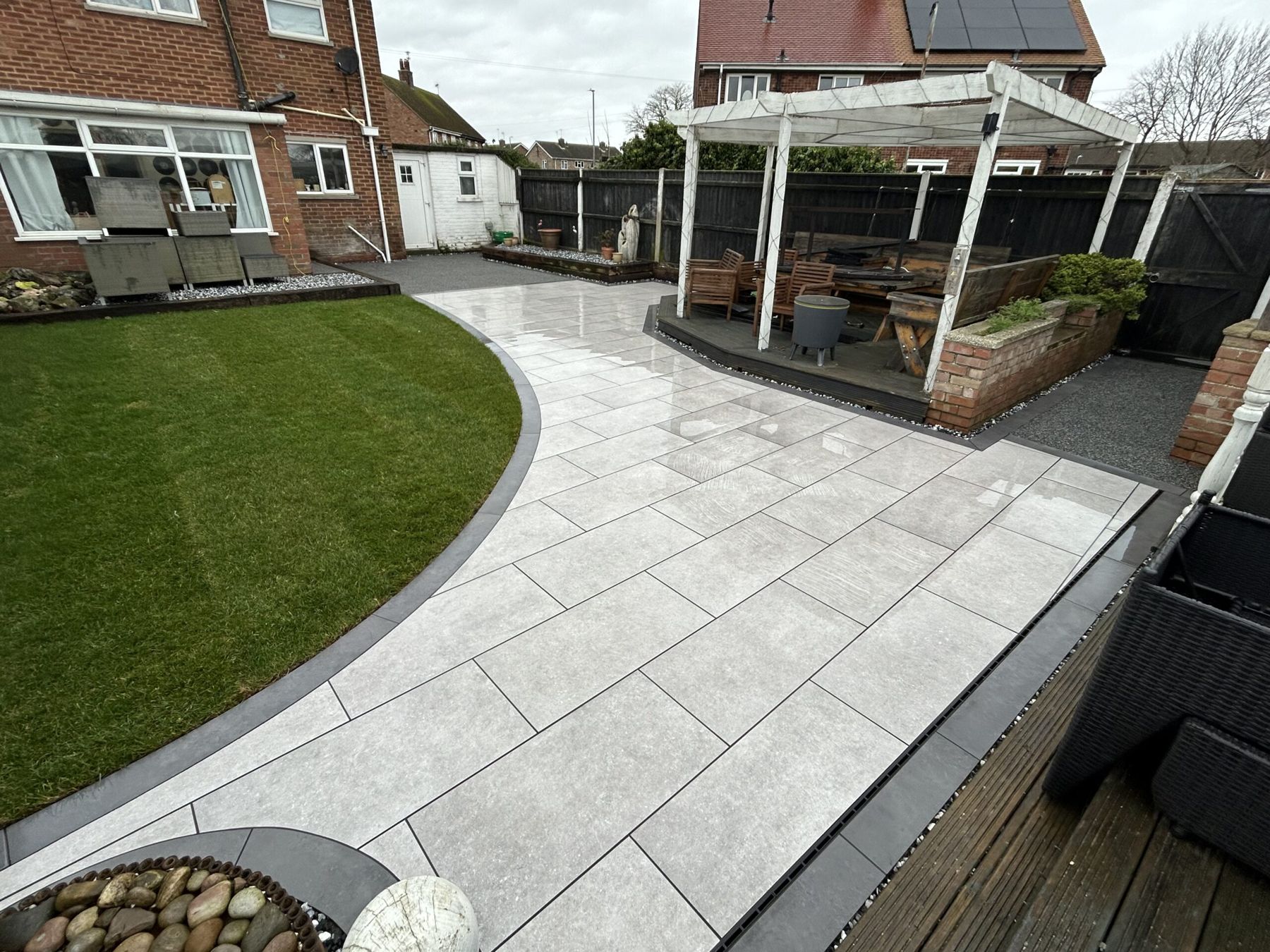 Curved grey porcelain patio between a lawn and a pergola