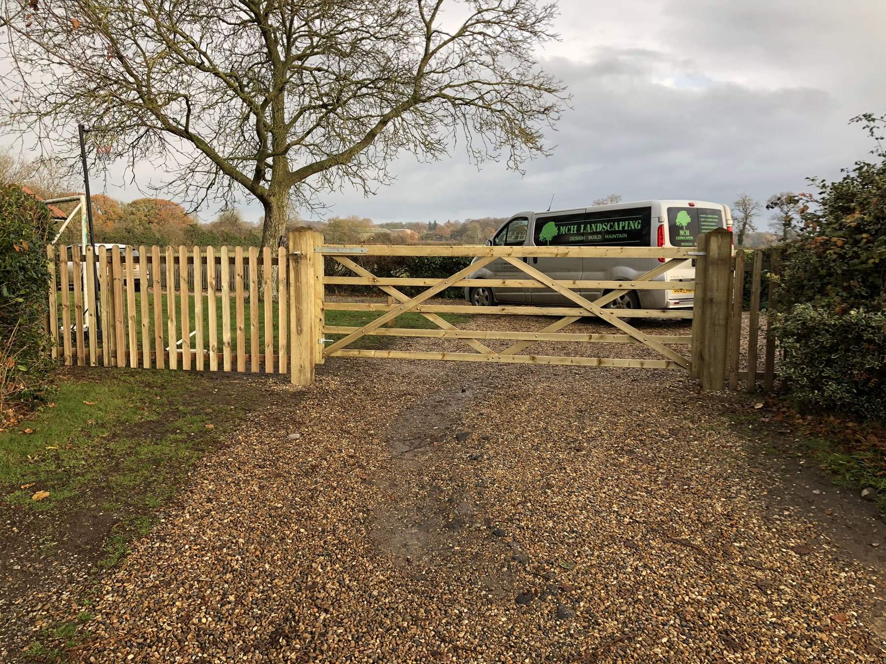 Gravel driveway leading to a timber five-bar gate and picket fencing