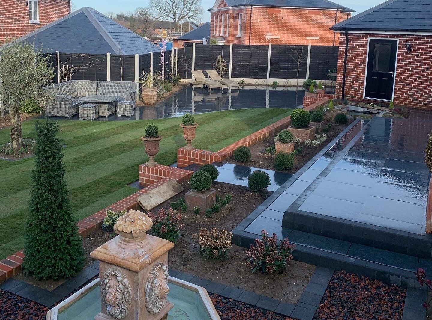 Formal garden with a striped lawn, topiary, dark paving and a water feature