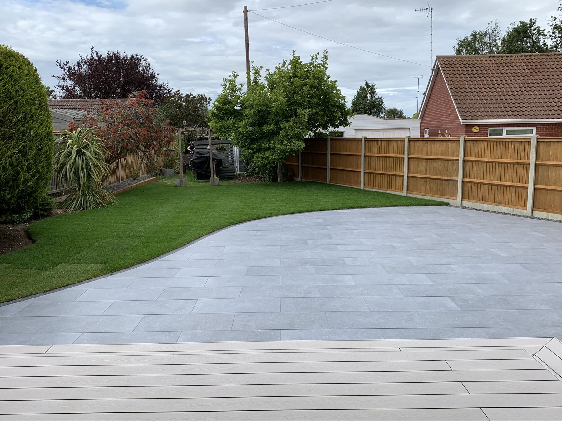 Grey porcelain patio curving into a lawn, with composite decking in front