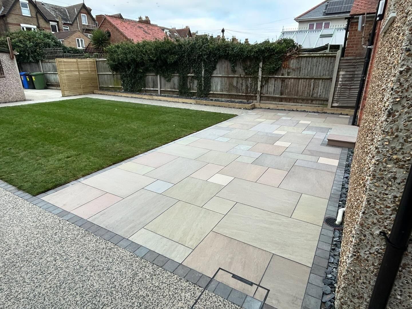 Natural stone patio meeting a new lawn, with a gravel edge and timber fencing