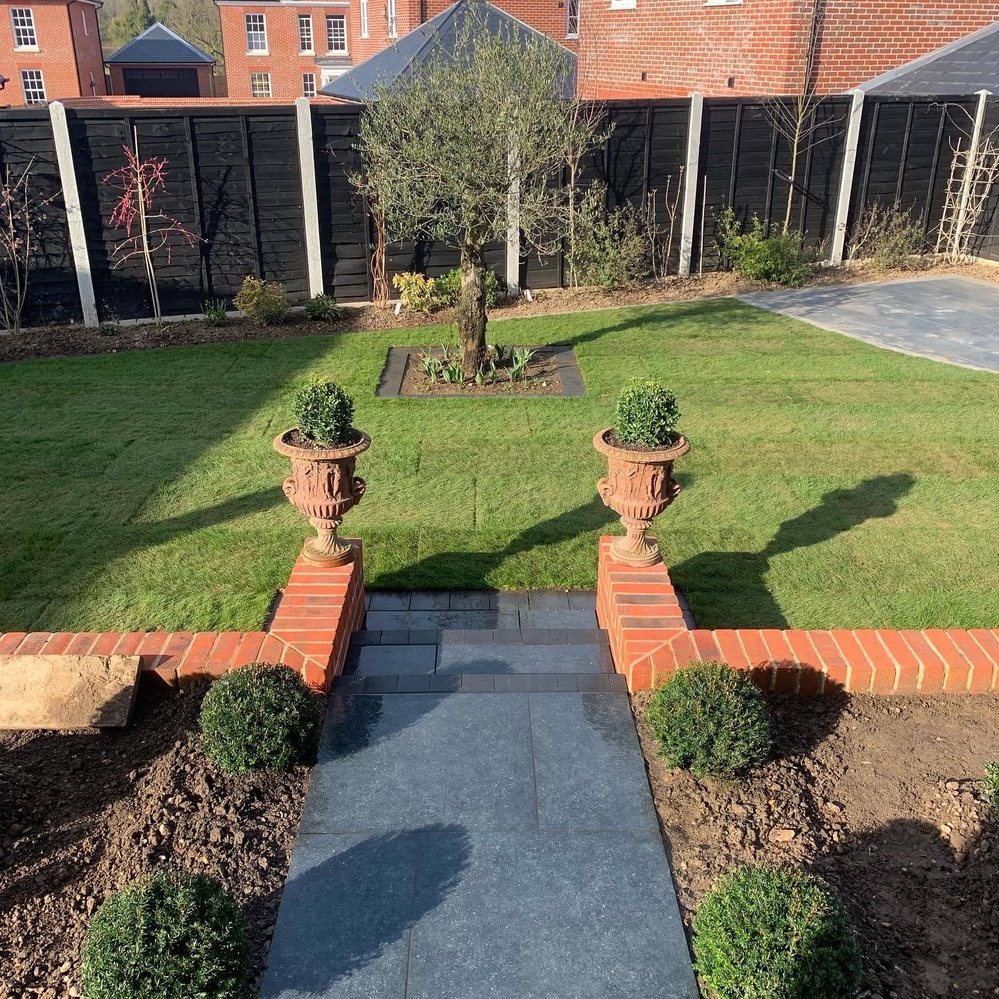 Path between lawns with stone urns and box planting