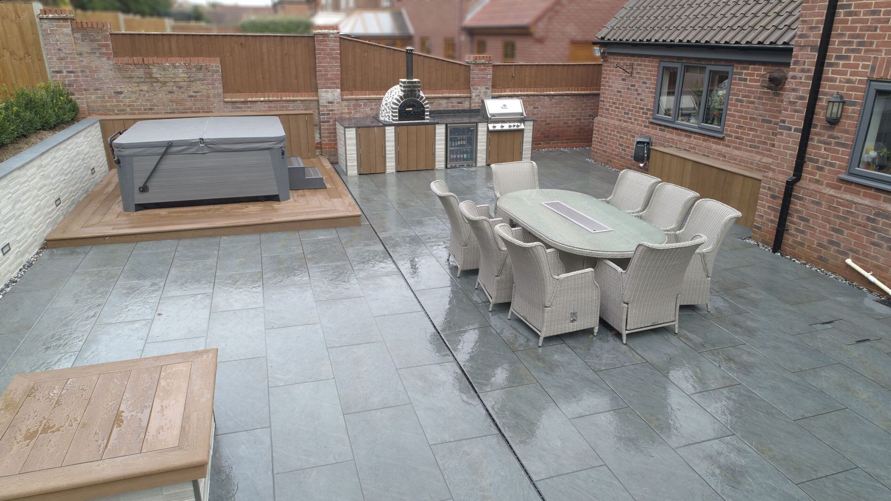 Grey porcelain patio with an outdoor kitchen, hot tub and dining set