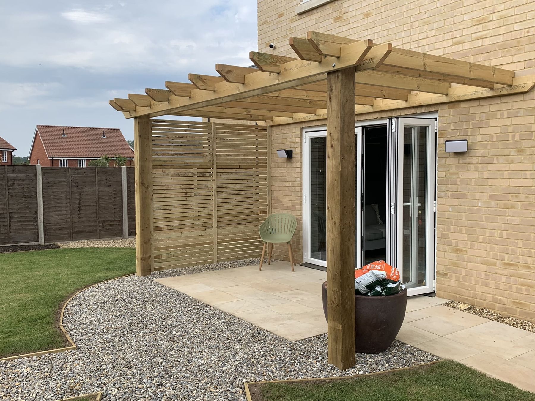 Pergola with slatted screening over a small patio and gravel