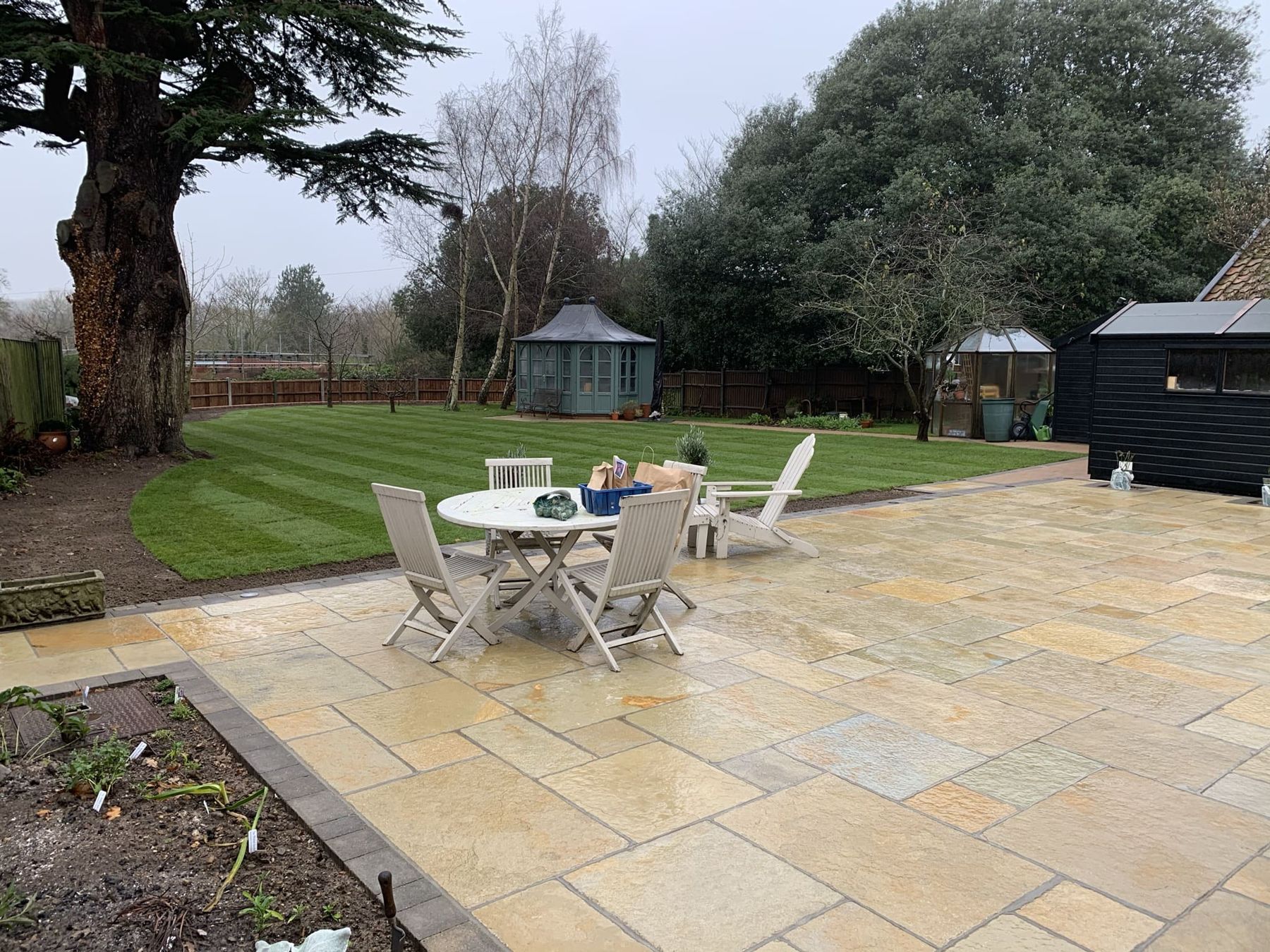 Sandstone patio with a round table and chairs beside a lawn and borders
