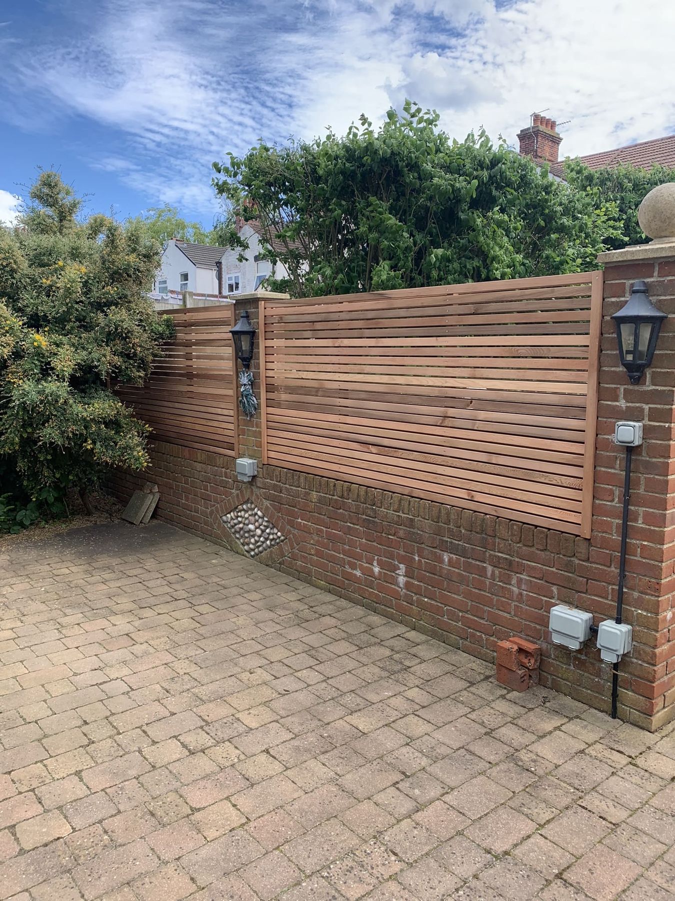 Slatted screening fixed above a brick wall over block paving
