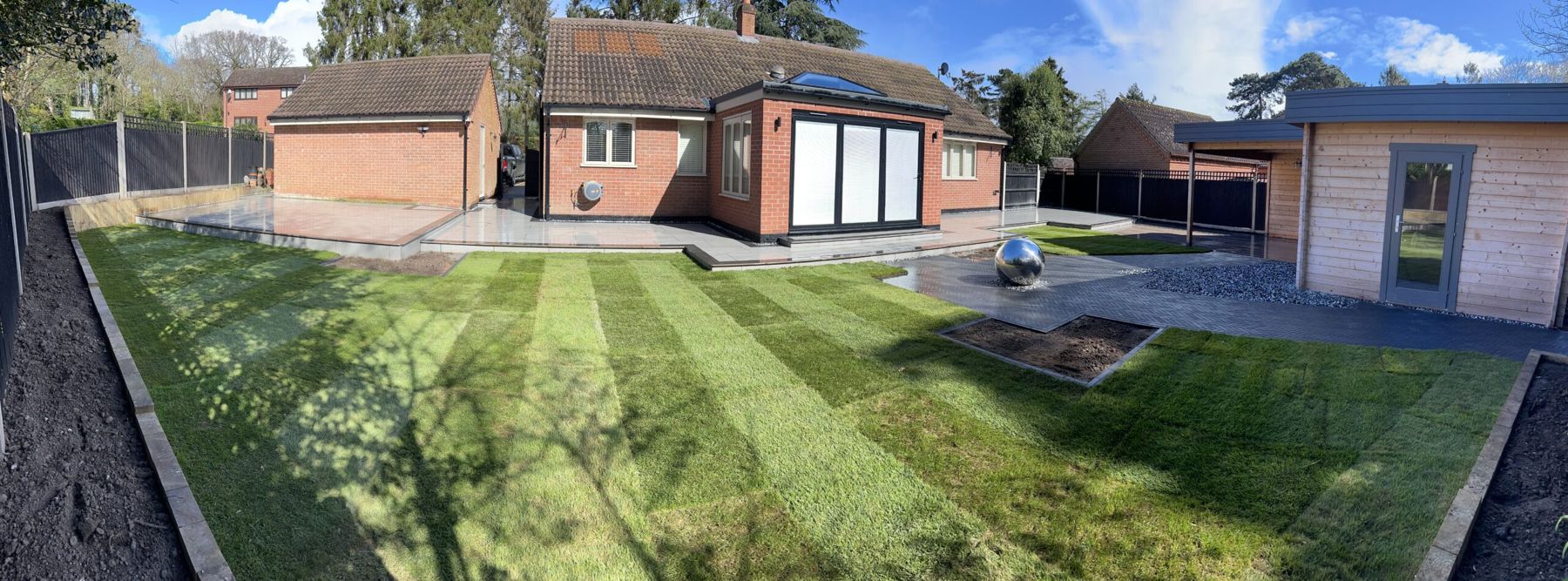 Wide striped lawn with a patio, a bungalow and a garden room