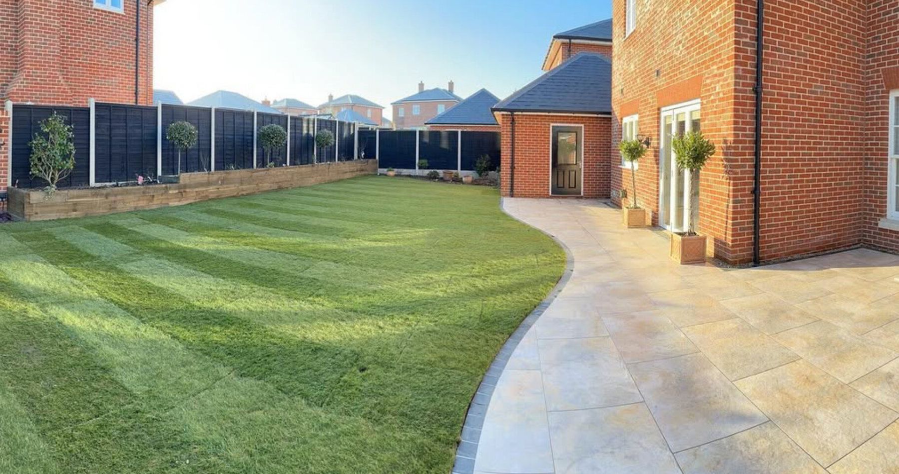 Striped lawn with a curving sandstone path beside a brick house