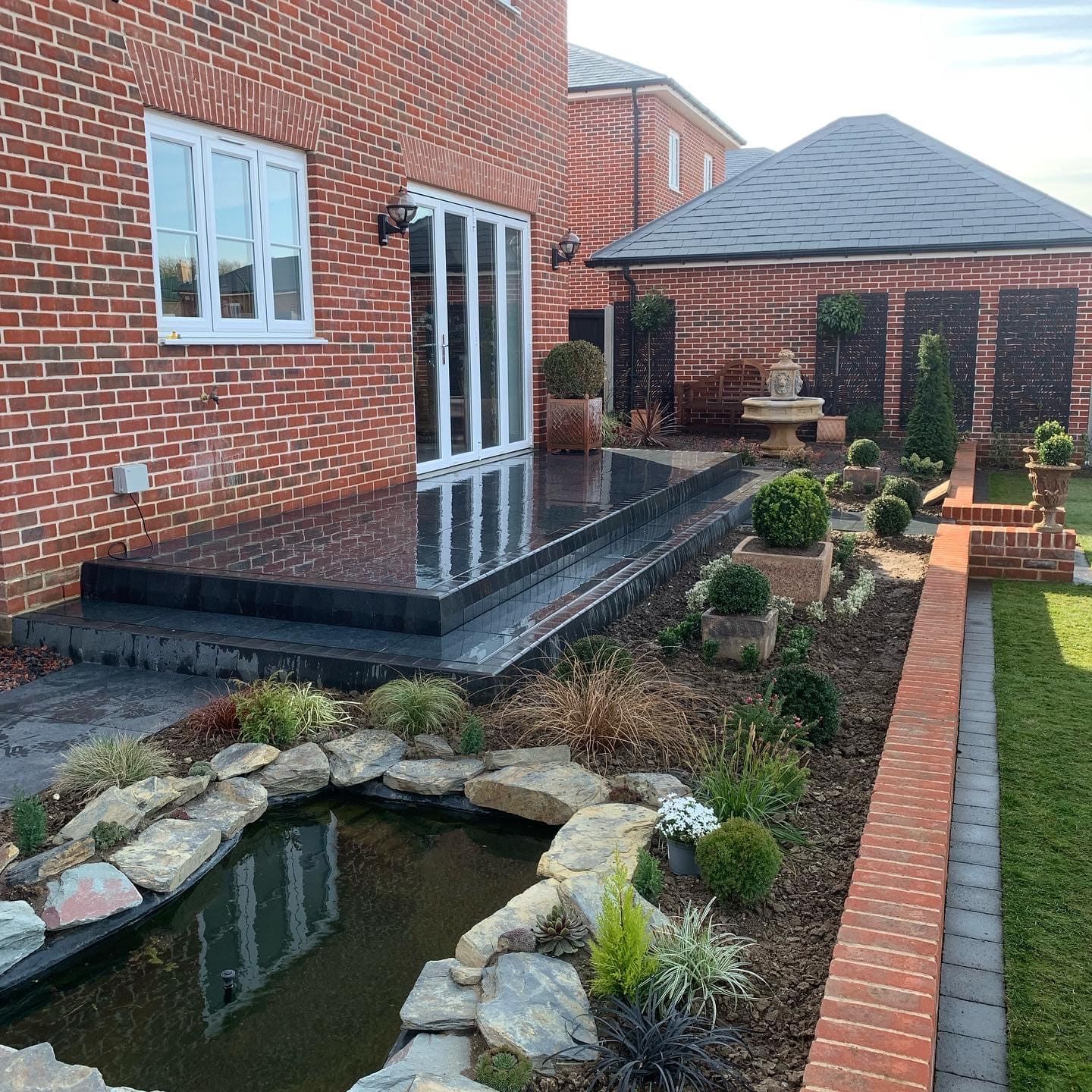 Raised dark porcelain terrace with a pond and rockery planting
